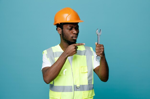 Pensando giovane costruttore afroamericano in tenuta uniforme e punti alla chiave aperta isolata su sfondo blu