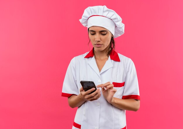 Pensando giovane donna cuoco che indossa il numero di composizione uniforme del cuoco unico sul telefono con lo spazio della copia