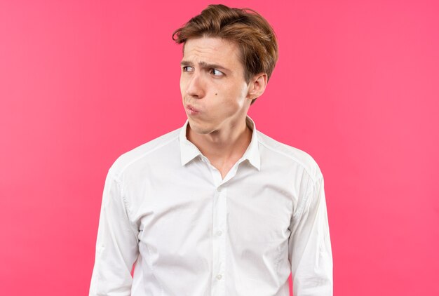 Pensando guardando lato giovane bel ragazzo che indossa una camicia bianca isolata sul muro rosa