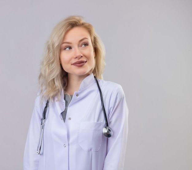 Pensando medico giovane ragazza che indossa uno stetoscopio in abito medico guardando a lato su sfondo bianco