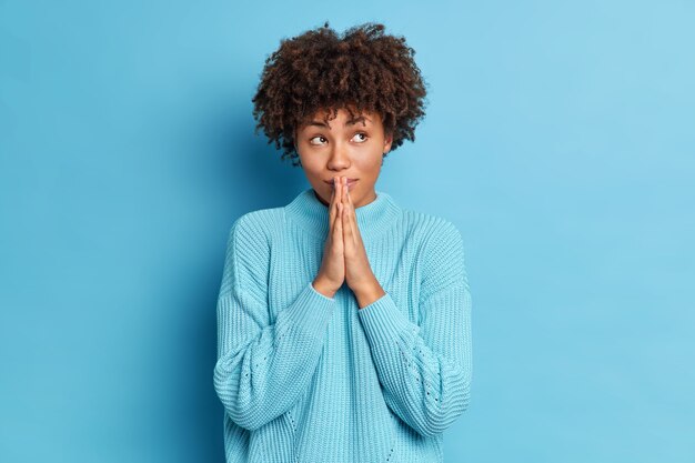 Pensierosa giovane ragazza dalla pelle scura con i capelli afro tiene i palmi premuti insieme e prega Dio crede in qualcosa di buono ha fede per una vita migliore vestita casualmente