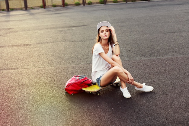 Pensieroso ragazza seduta su skateboard al tramonto