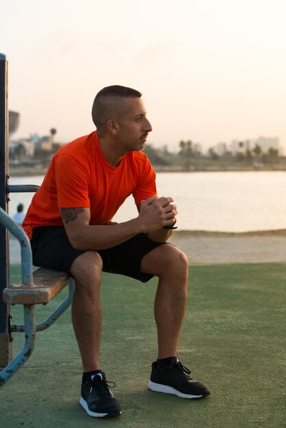 Pensive giovane atleta maschio seduto sul parco giochi