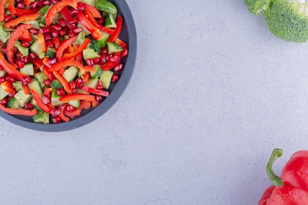 Pentola nera di insalata di verdure accanto a un peperone e un broccolo su sfondo marmo. Foto di alta qualità