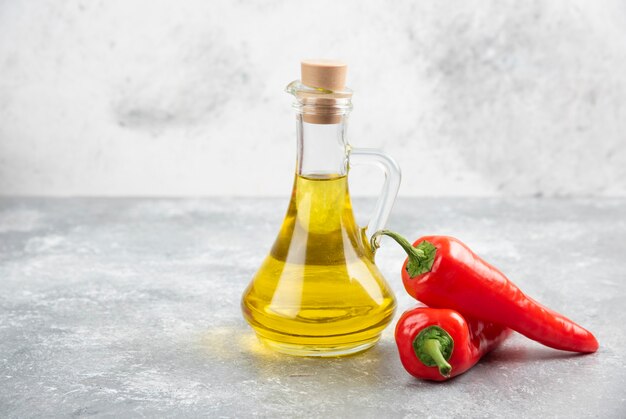 Peperoncini rossi con una bottiglia di olio extra vergine di oliva sul tavolo di marmo.