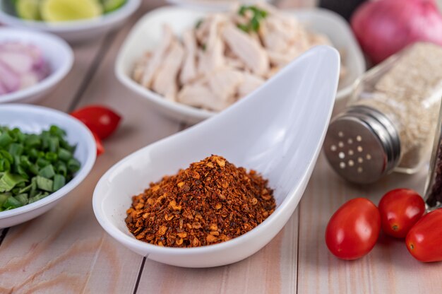 Peperoncino di cayenna in un cucchiaio bianco, pomodoro disposto su una tavola di legno.