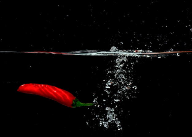 Peperoncino rosso che cade con le bolle nell&#39;acqua contro fondo nero