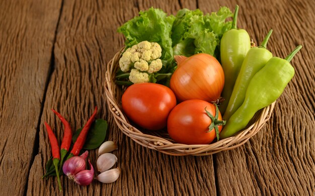 Peperone, pomodoro, cipolla, insalata, peperoncino, scalogno, aglio, cavolfiore e foglie di lime kaffir su un cestino di legno sul tavolo di legno