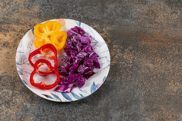 Peperoni dolci affettati e cavolo rosso tritato finemente nel piatto, sulla superficie del marmo