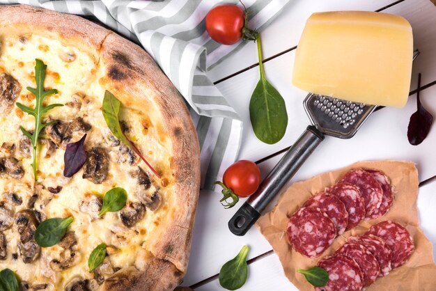 Peperoni freschi con verdure; formaggio; grattugia e deliziosa pizza su pannello di legno