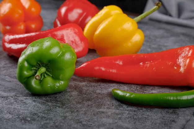 Peperoni freschi e colorati su un tavolo di pietra grigia.