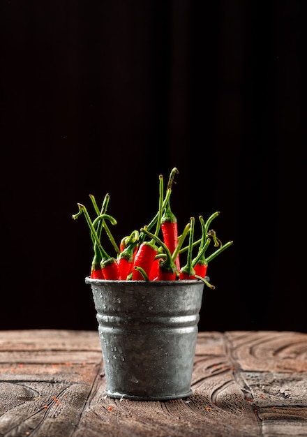 Peperoni in un mini secchio su piastrelle di pietra e sfondo nero.