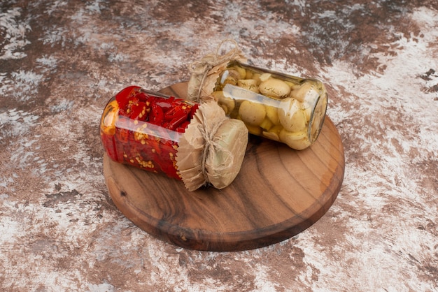 Peperoni rossi marinati e funghi in un barattolo di vetro sul piatto di legno.