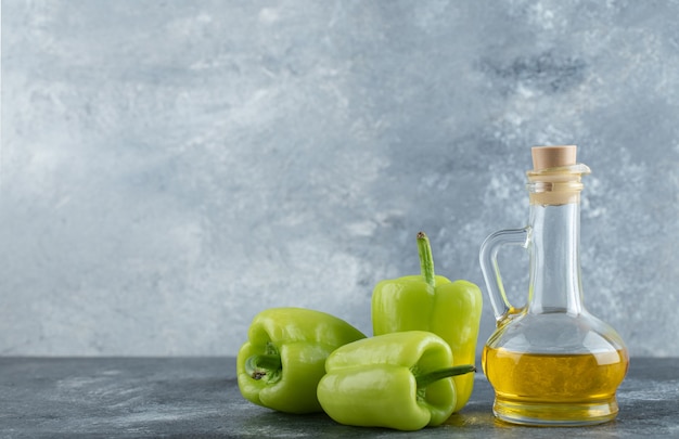 Peperoni verdi organici freschi con bottiglia di olio su sfondo grigio.
