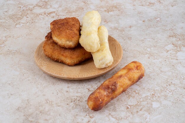 Pepite croccanti, bastoncini di formaggio e salsicce alla griglia su un piatto di legno.