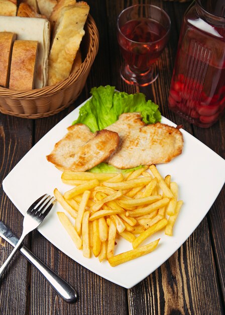 Pepite di petto di pollo arrosto con patatine fritte nel piatto bianco.