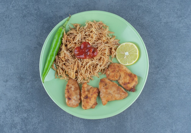 Pepite di pollo e pasta fritta sul piatto verde.