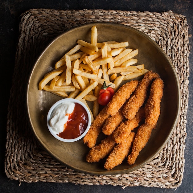 Pepite di pollo vista dall'alto con patatine fritte e pomodoro e sous in piatti di argilla