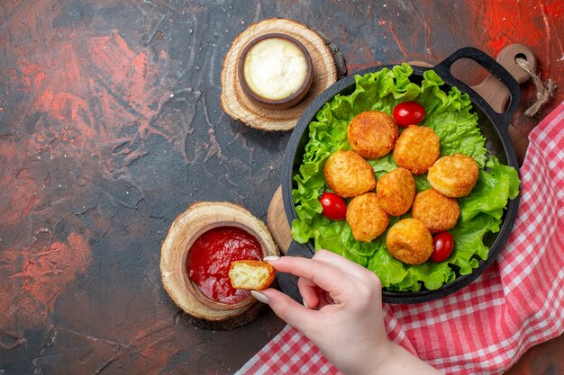 Pepite di pollo vista dall'alto e salse sul tagliere pepite in mano della donna sul muro rosso scuro