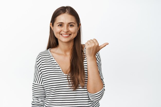 Per di qua. Ragazza sorridente che mostra la direzione, punta il dito a destra e sembra felice, consiglia negozio o banner di vendita su bianco