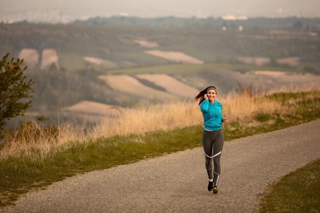 Per tutta la lunghezza del corridore femminile che ascolta musica mentre fa jogging sulla strada all'alba