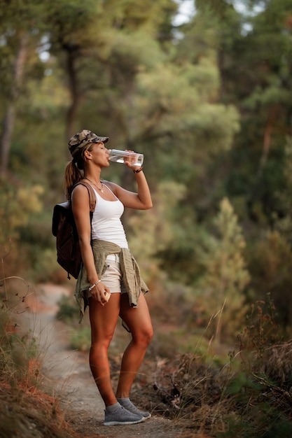 Per tutta la lunghezza dell'acqua potabile dell'escursionista femminile mentre si sta in piedi su un sentiero nella foresta