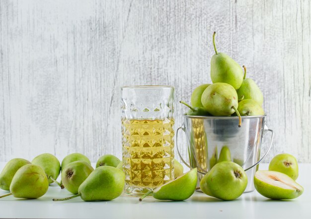 Pere con bevanda in un mini secchio sulla parete bianca e sgangherata, vista laterale.