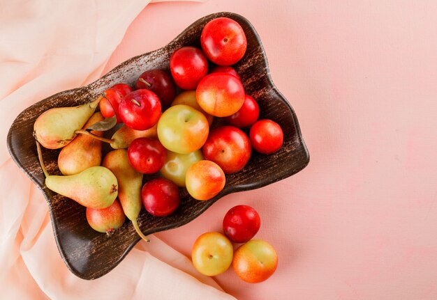 Pere e prugne in un piatto sulla superficie del tessuto e rosa