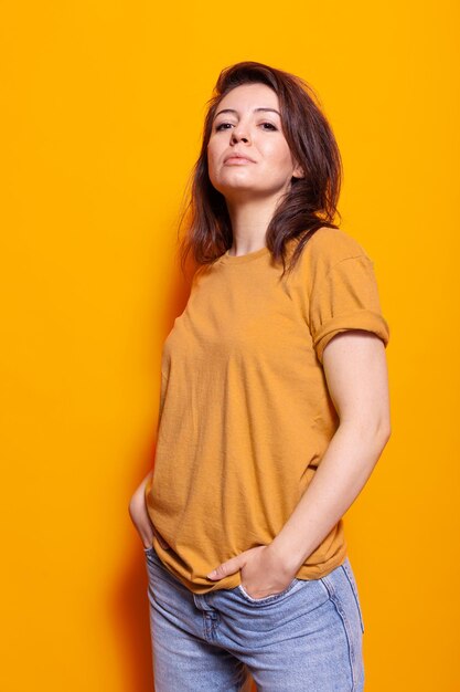 Persona allegra in piedi su sfondo arancione in studio. Donna allegra che posa con sicurezza, sentendosi casual mentre guarda la macchina fotografica. Elegante adulto sorridente e con le mani in tasca