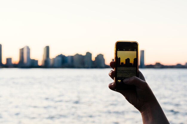 Persona che cattura foto del tramonto della città su smartphone