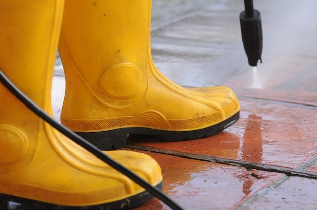 Persona che indossa stivali di gomma gialli con ugello dell'acqua ad alta pressione che pulisce lo sporco nelle piastrelle