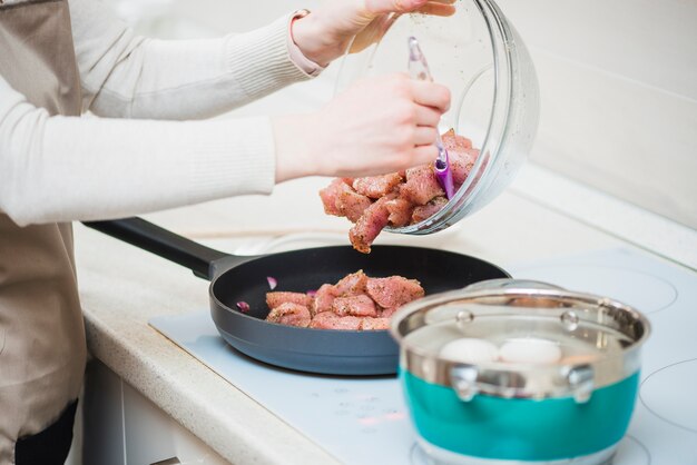 Persona che mette carne cruda in padella