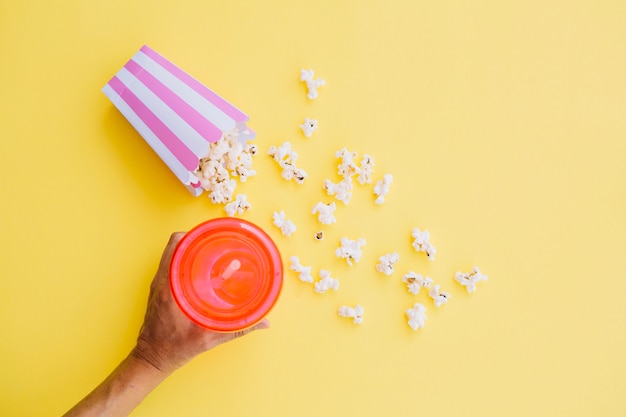 Persona che prende la tazza della bevanda vicino a popcorn rovesciato