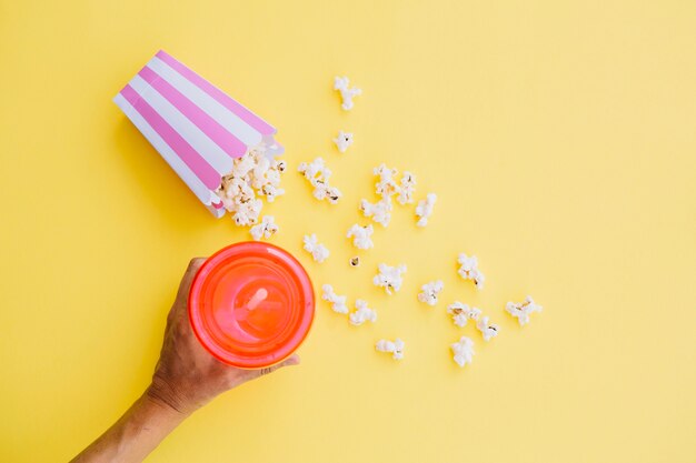 Persona che prende la tazza della bevanda vicino a popcorn rovesciato