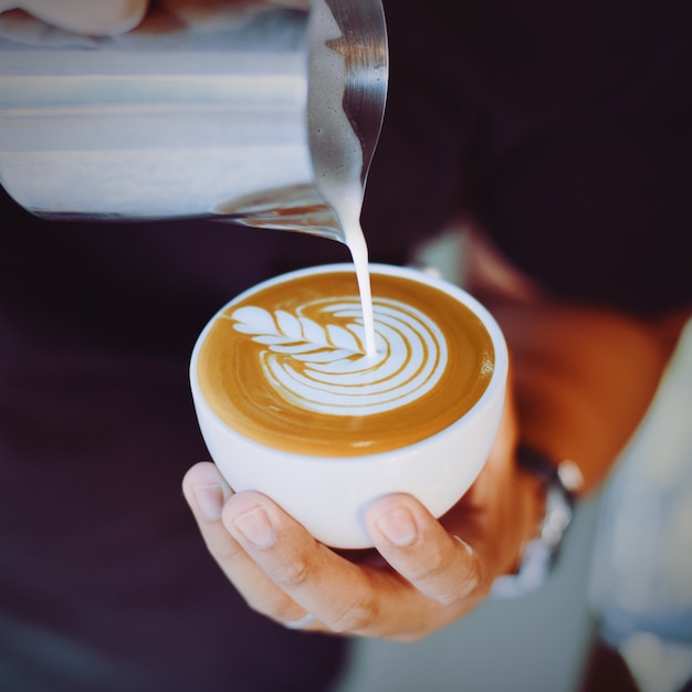 Persona che serve una tazza di caffè con una brocca di metallo