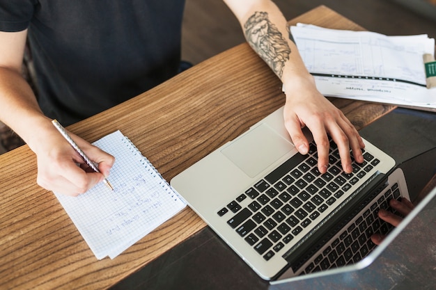 Persona che si siede con il computer portatile e blocco note al tavolo