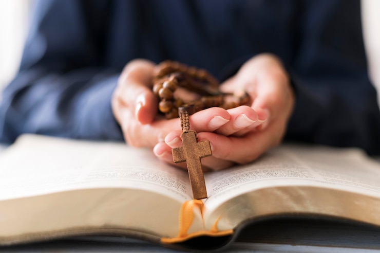 Foto gratuito persona che tiene il rosario con croce sul libro sacro aperto