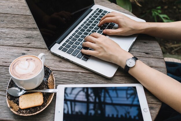 Persona che utilizza computer portatile vicino a caffè e tablet