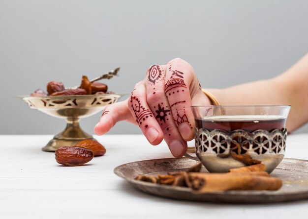 Persona con mehndi che tiene tazza di tè sul tavolo