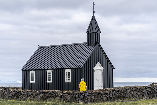 Persona con un cappotto giallo seduto su un muretto davanti alla Buoir in Islanda