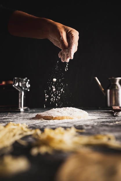 Persona del primo piano che spruzza farina su pasta