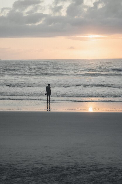 Persona in piedi da sola su una spiaggia con il riflesso di un sole al tramonto