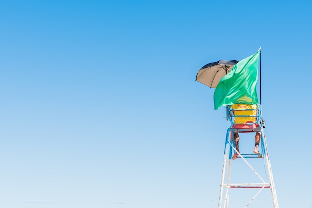 Persona in piedi sul sedile di sicurezza in spiaggia con una bandiera verde sventolante