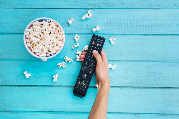 Persona in possesso di telecomando vicino secchio di popcorn