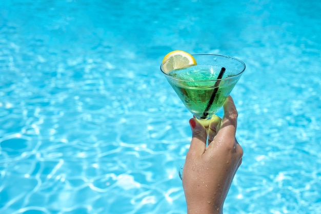 Persona in possesso di un bicchiere di delizioso cocktail verde in una piscina sotto la luce del sole