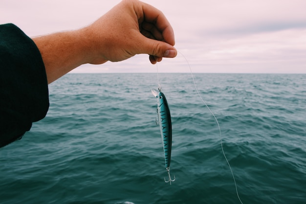 Persona in possesso di un'esca da pesca con il mare e un cielo nuvoloso