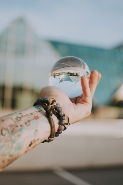 Persona in possesso di una sfera di cristallo trasparente con il riflesso di un edificio triangolare
