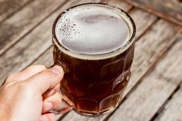 Persona in possesso di una tazza di vetro di birra fredda con una superficie in legno