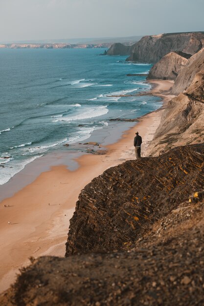 Persona su una scogliera guardando il bellissimo oceano in Algarve, Portogallo