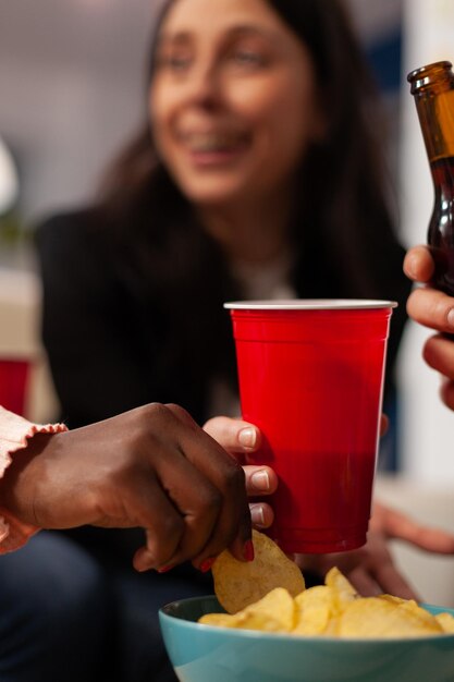 Persone allegre che si godono la festa in ufficio con bevande e spuntini dopo l'orario di lavoro. I colleghi mangiano patatine dalla ciotola, tengono bicchieri e bottiglie di birra, fanno attività divertenti. Avvicinamento.